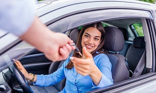 Woman in driver's seat of car being handed the key to rental car through window